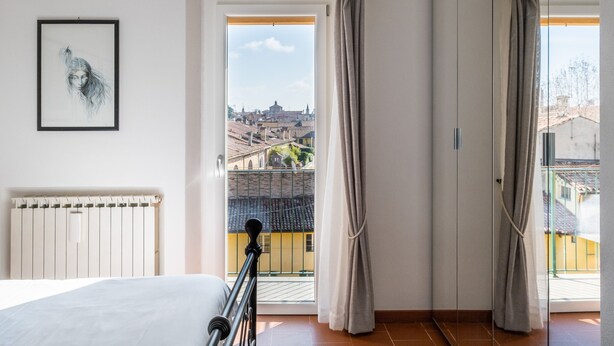 A bedroom with a bed, a radiator, a framed artwork, and a balcony with curtains.