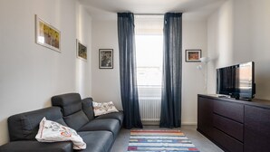 A modern living room with a sofa, a television on a cabinet, and a window with curtains.