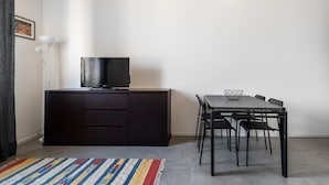 A modern living space with a flat-screen TV on a dark wooden cabinet, a dining table with four chairs, and a colorful striped rug.