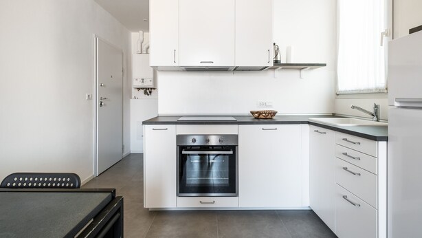 A modern kitchen with white cabinets, a built-in oven, and a black countertop.