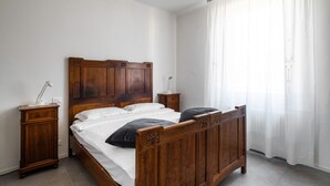 A bedroom with a wooden bed, two bedside tables, and a window with sheer curtains.