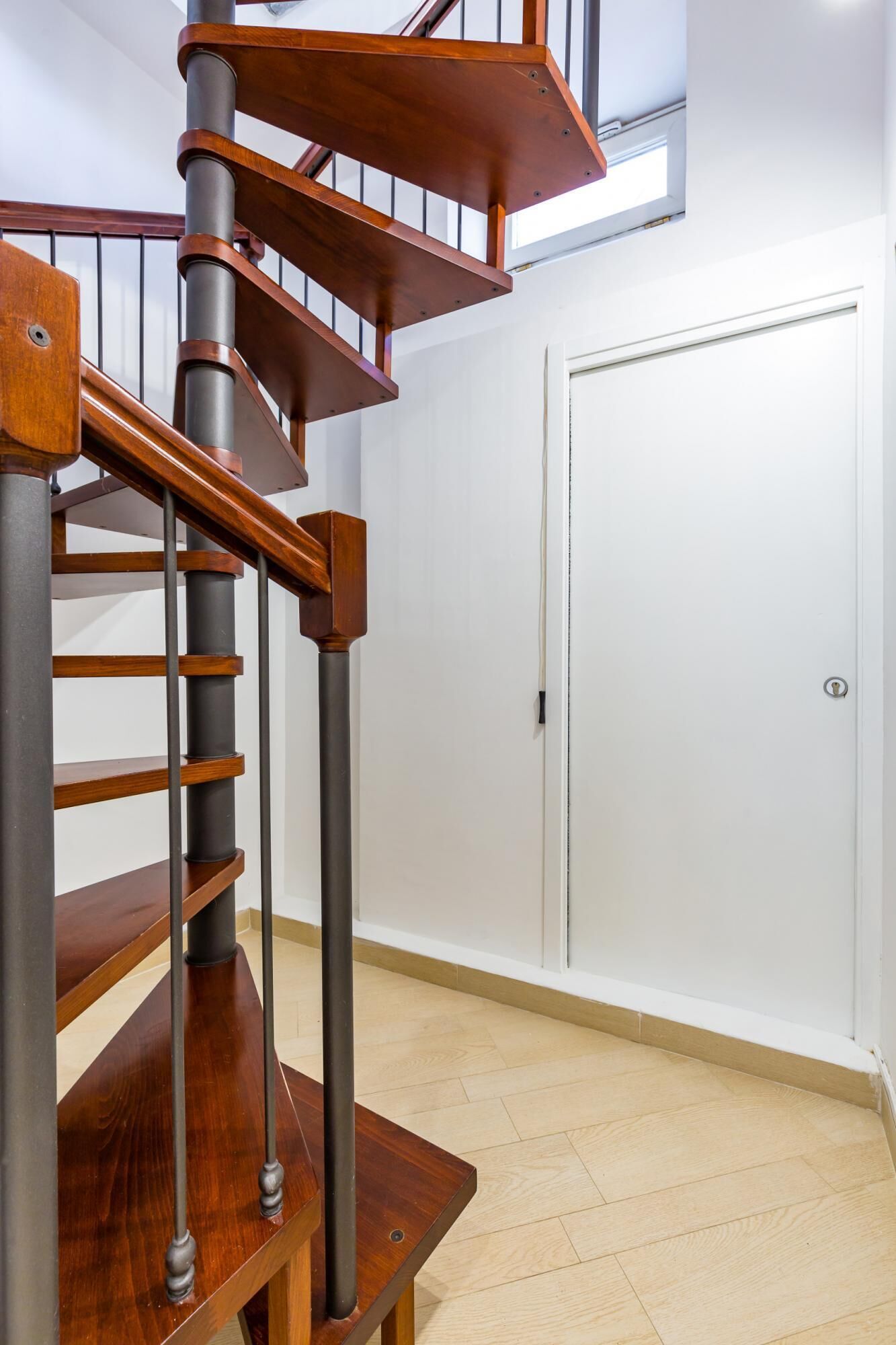Un escalier en colimaçon avec des marches en bois et des rampes en métal, menant à une porte blanche.