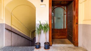 Un escalier avec une rampe, deux plantes en pot, un luminaire fixé au mur et une porte en bois avec un panneau de verre.