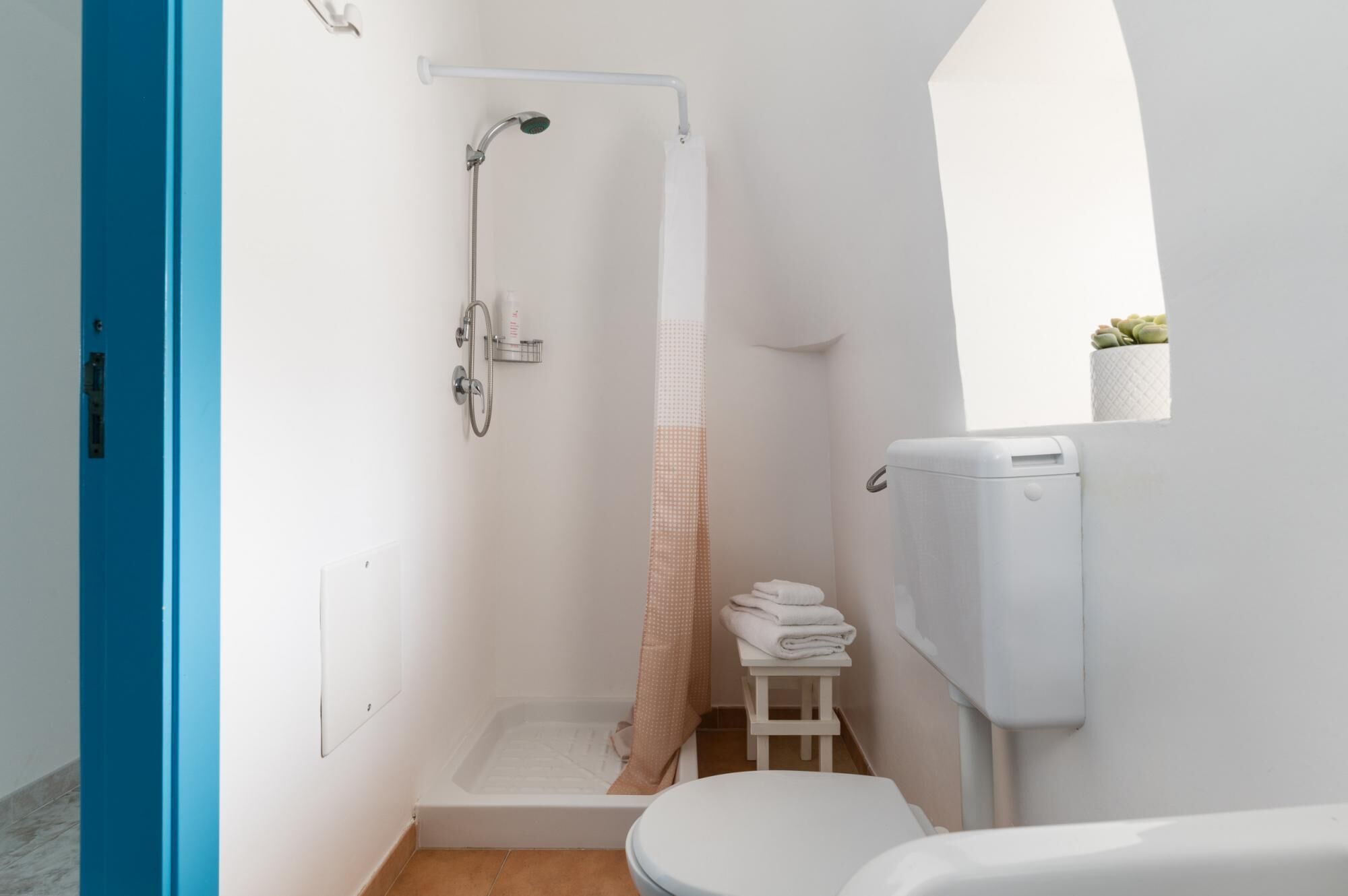 Casa de banho pequena e moderna com chuveiro, sanita e um pequeno banquinho.