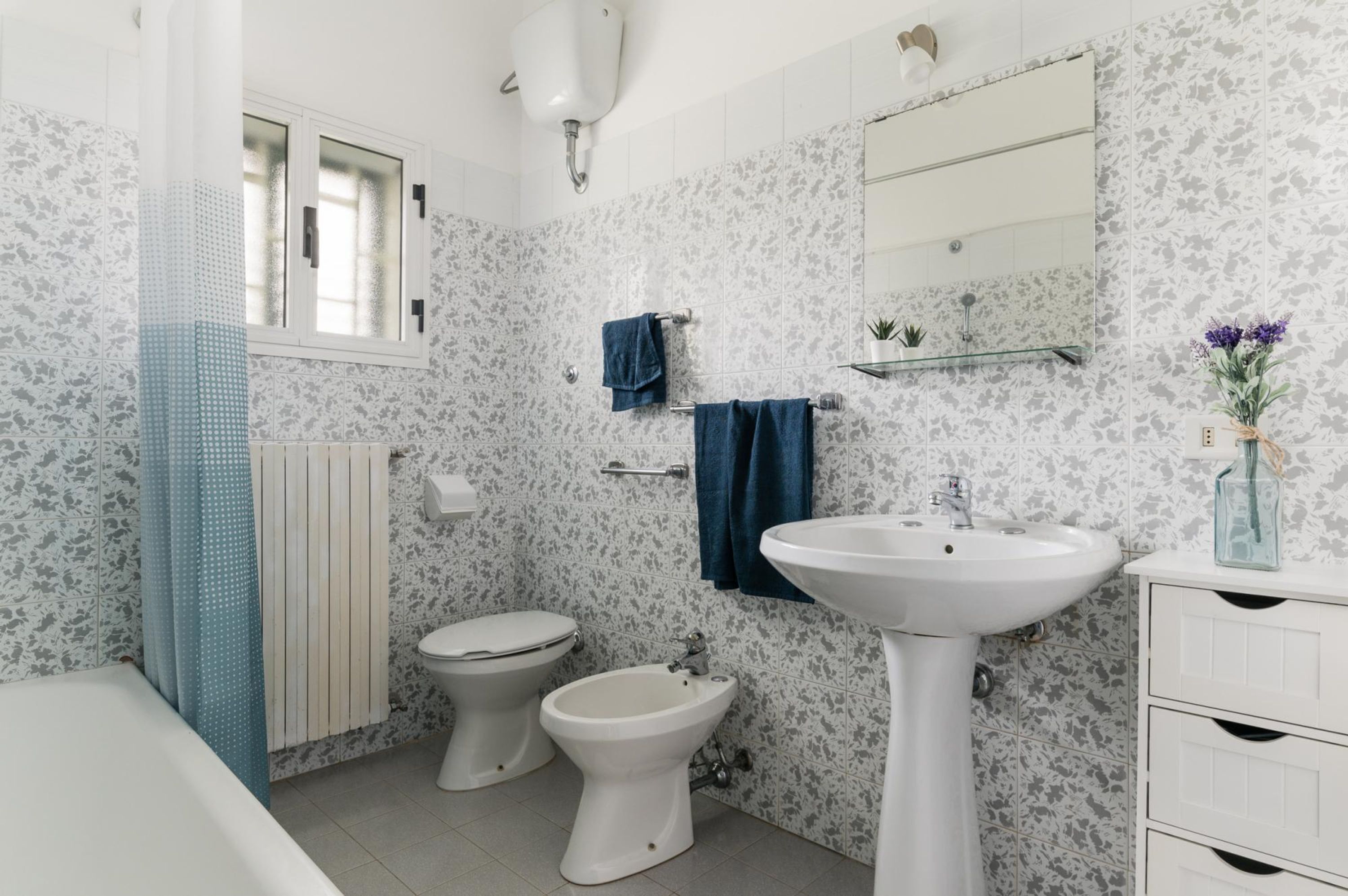 A bathroom with a toilet, bidet, sink, and a window.