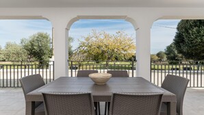 A covered patio with a table and chairs, a large bowl, and a view of a park with trees and a fence.