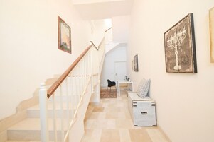 Un pasillo con una escalera de madera, una puerta blanca al final y una pequeña mesa con una silla.