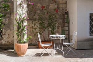 Un patio con una mesa, dos sillas, una planta en maceta y una pared cubierta de plantas trepadoras.