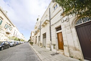 Una calle empedrada flanqueada por edificios históricos, coches aparcados y un cielo despejado.