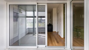 A modern interior with a glass door leading to a balcony, a wooden floor, and a view of a building and trees. - Casa Bassani con Terrazzo by Wonderful Italy (Bologna)