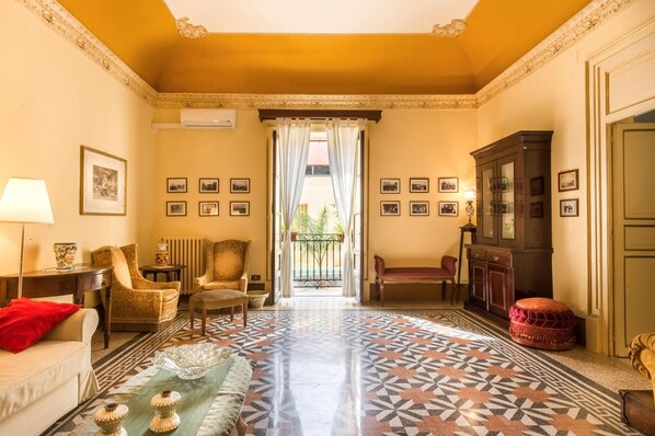 A room with a patterned floor, a sofa, armchairs, a cabinet, and a view through a doorway. - Casa Ugdulena con Piscina by Wonderful Italy (Palermo)