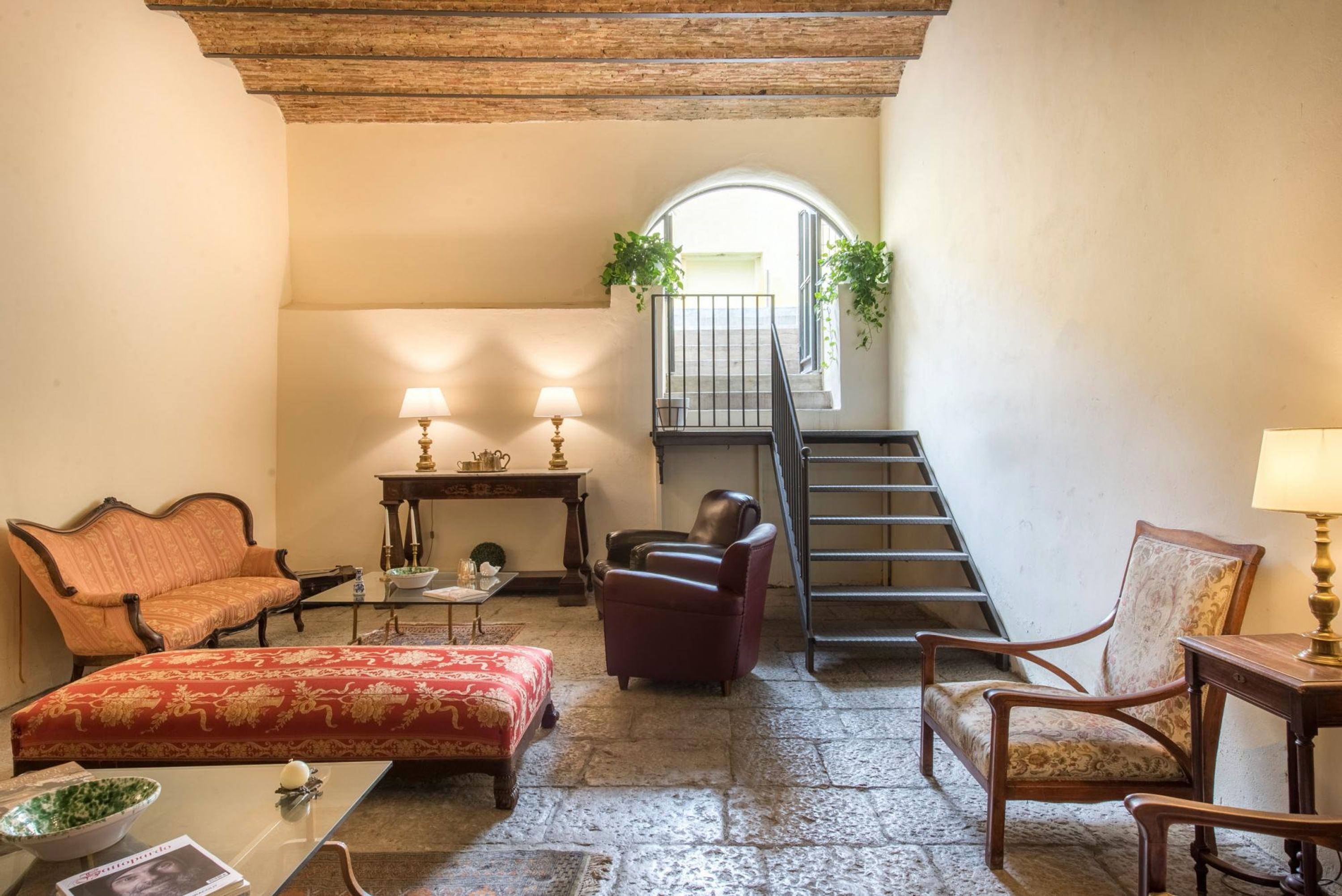 A cozy room with a sofa, armchairs, a table, and a staircase leading to an upper level.