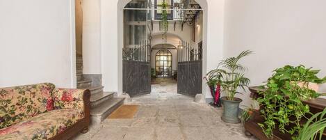 A spacious hallway with a floral sofa, potted plants, and a staircase leading to an upper level.