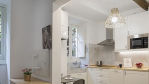 A modern kitchen with white cabinetry, a stainless steel range hood, a microwave, and a hanging light fixture. - Cozy Holiday Home in Camogli (Camogli)