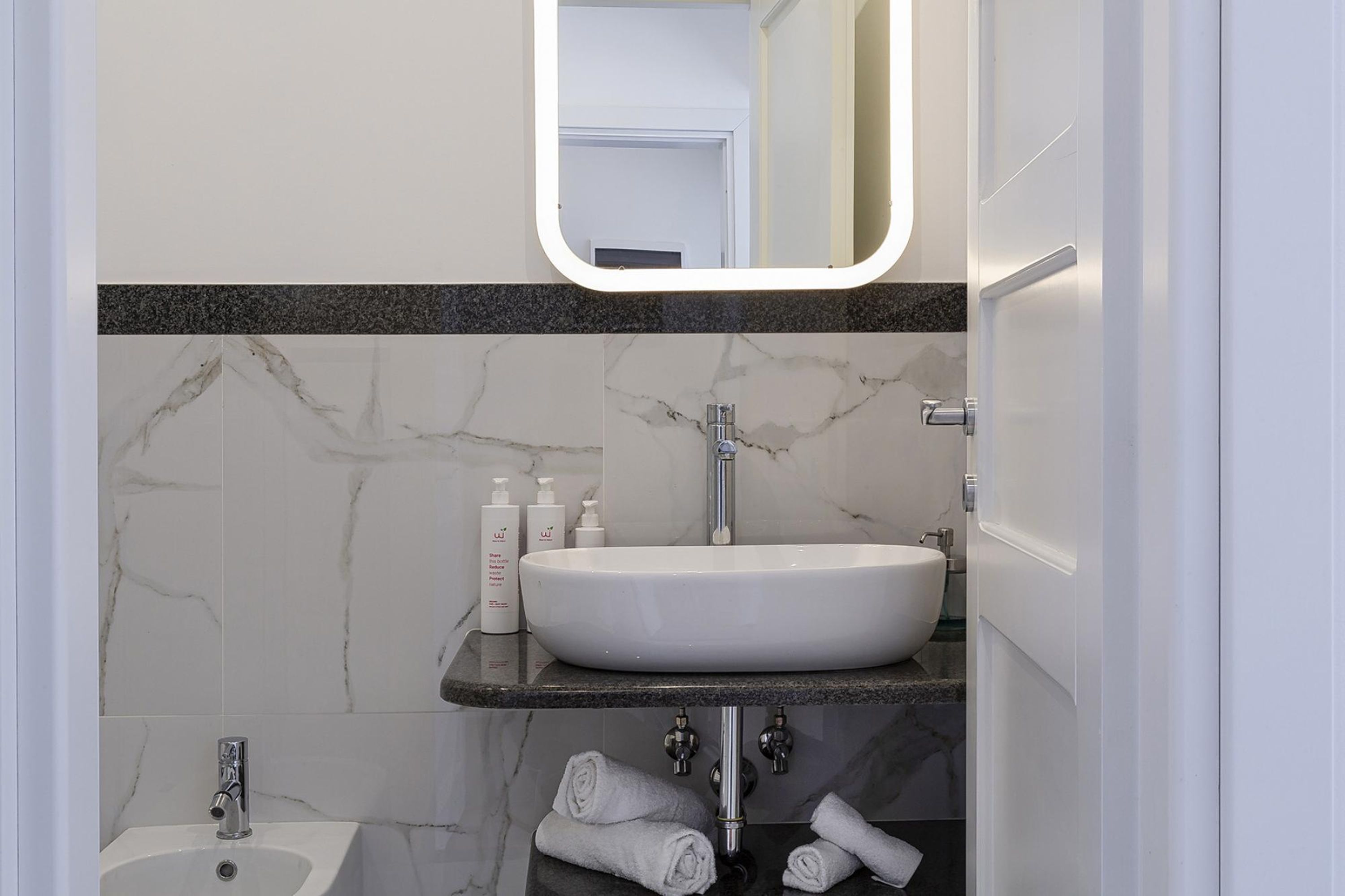 A modern bathroom with a white sink, marble walls, and a black countertop.