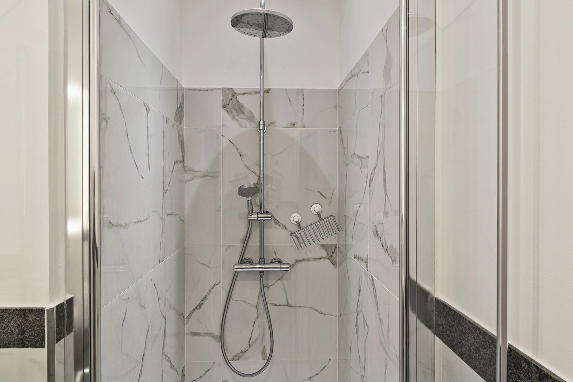 Ducha envuelta en vidrio con cabezal de ducha de mano, grifo de pared y ducha de lluvia.