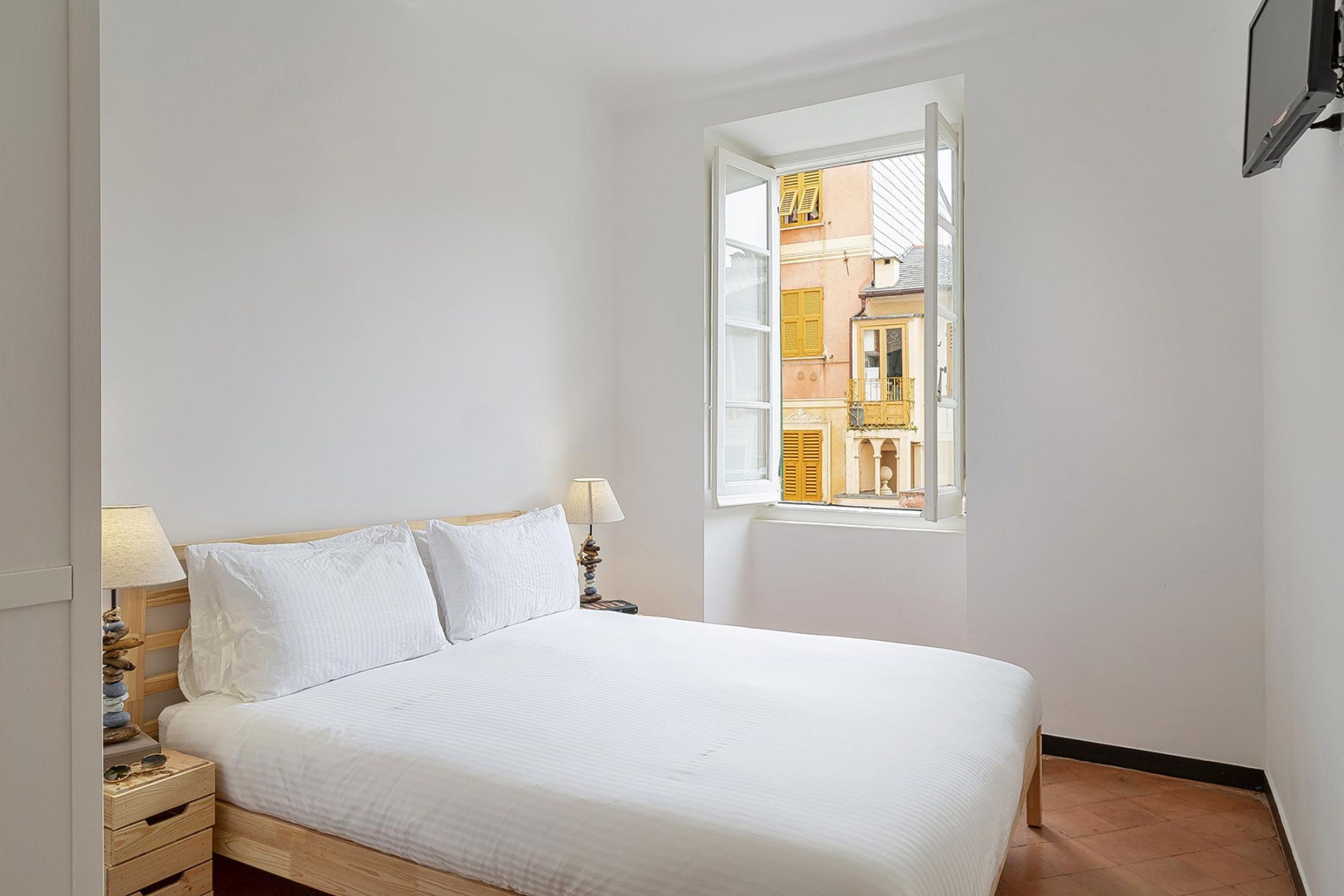 A bedroom with a bed, two bedside lamps, a nightstand, and a window with a view of buildings.