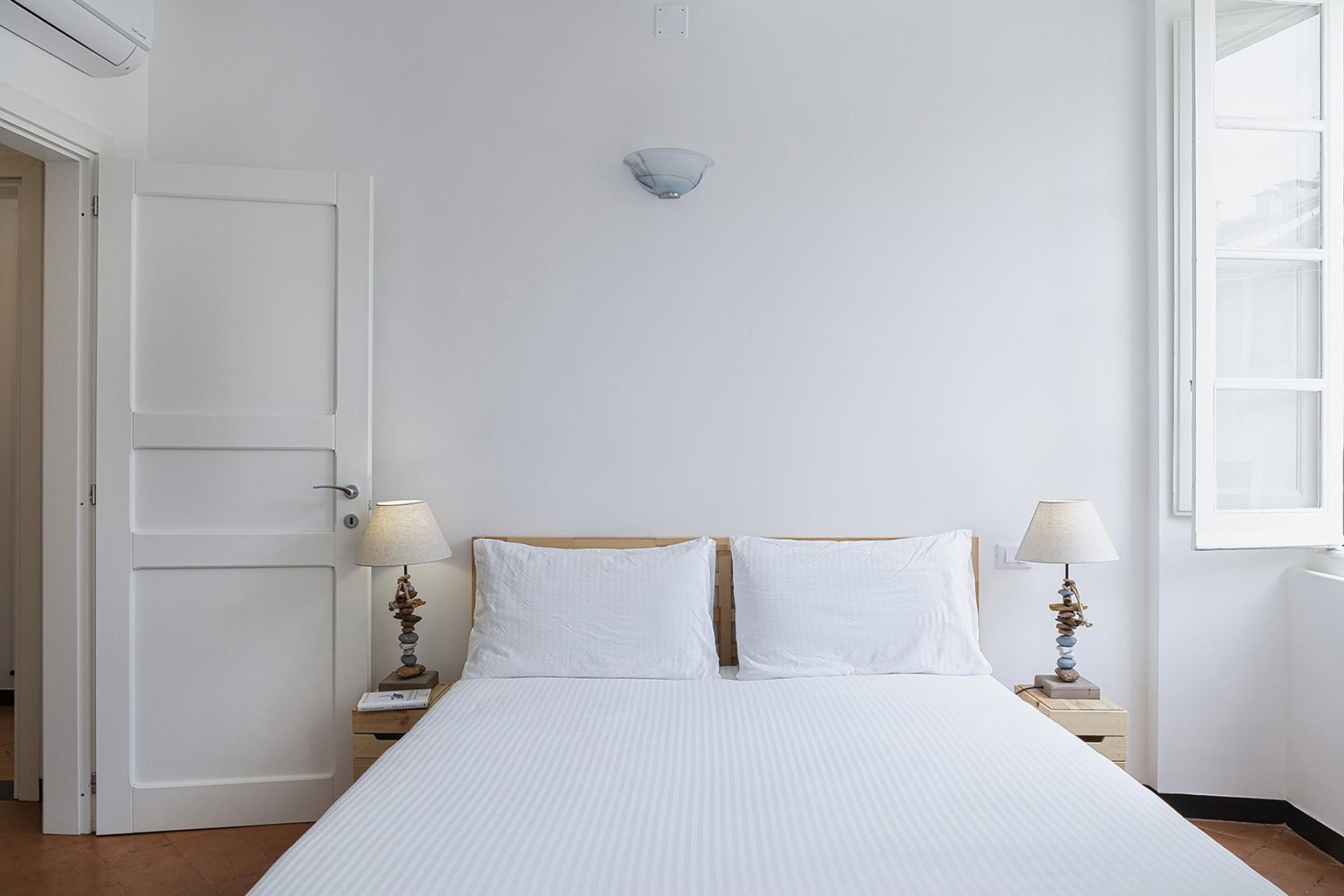 A bedroom with a bed, two bedside lamps, a wall-mounted light fixture, and a window.