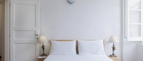 A bedroom with a bed, two bedside lamps, a wall-mounted light fixture, and a window.