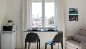 A small dining area with a table set for two, a microwave, and a plant on a small table. - Dioniso Smart Suite With Balcony by Wonderful Italy (Syracuse)