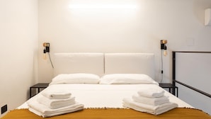 Habitación de hotel con cama, dos lámparas de pared y televisor de pantalla plana sobre un soporte.