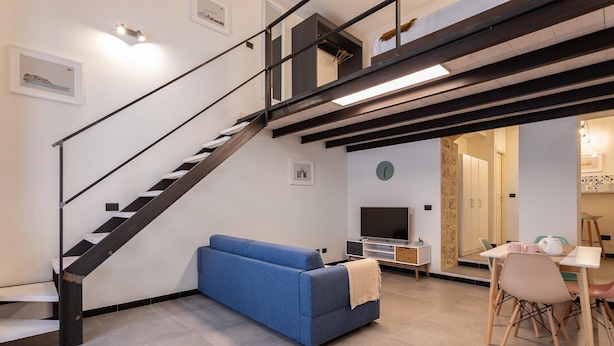 Una sala de estar moderna con un sofá azul, un comedor con mesa y sillas, y una escalera con barandales negros.