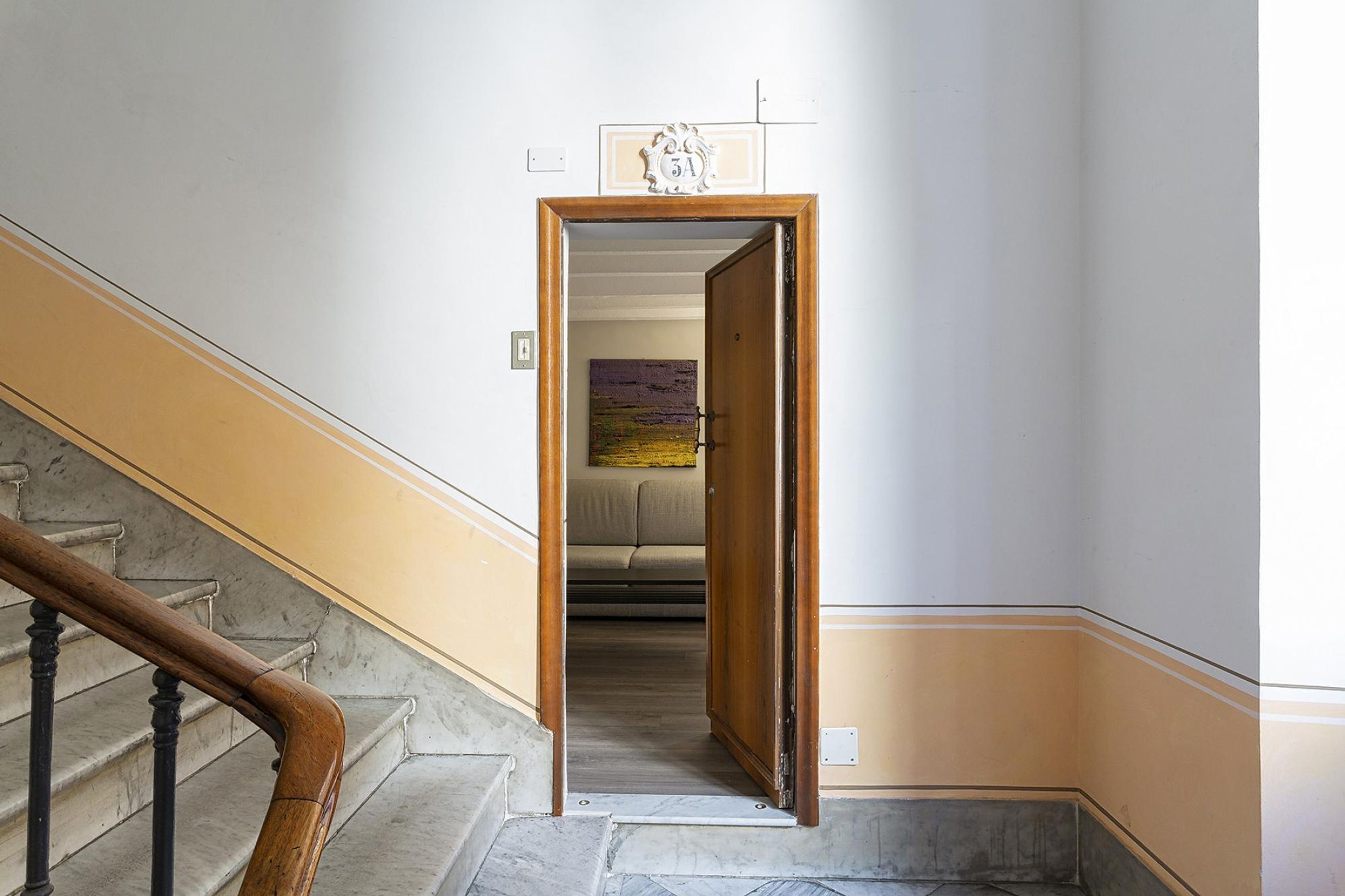 A hallway with a wooden door leading to a room with a bed and a painting on the wall.