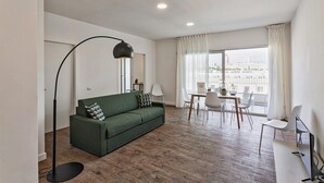 A modern living room with a green sofa, a dining table with chairs, a floor lamp, and a large window with curtains. - Deluxe Apartment - Grey by Wonderful Italy (Genoa)