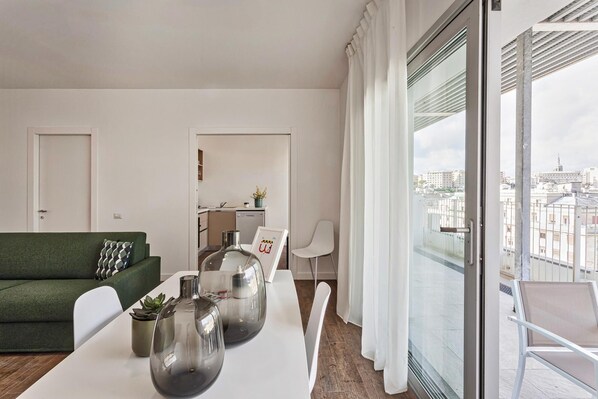 Een moderne woonkamer met een groene bank, een eettafel met drie glazen vazen en een keuken in de achtergrond.