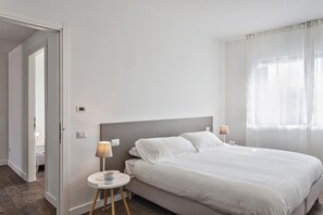 Een hotelkamer met een bed, bedlampen, een tafeltje en een deur naar een andere kamer.