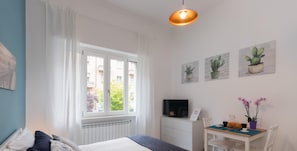 A bedroom with a bed, a desk, a chair, a TV, and a window with curtains. - Studio Glicine by Wonderful Italy (Turin)