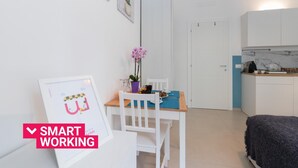 A small, bright room with a desk, chair, and a bed. There is a framed picture on the wall and a small table with a plant. - Studio Glicine by Wonderful Italy (Turin)