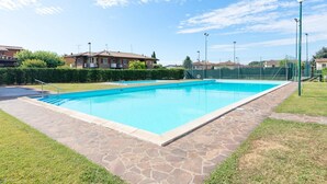 A rectangular swimming pool with stone tiles, surrounded by a grassy area and a hedge.