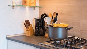 A kitchen with a gas stove, a pot of spaghetti, a coffee maker, and various utensils on the counter.