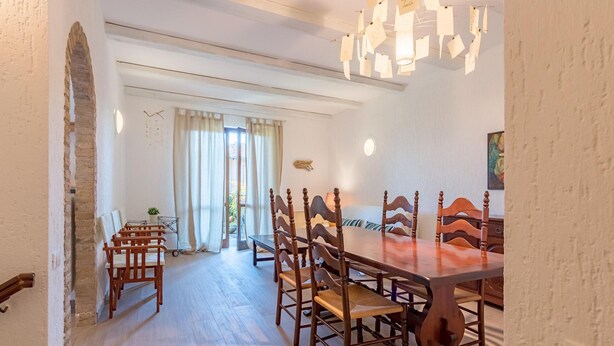 A dining area with a wooden table and chairs, a chandelier, and a view of the outdoors through a window with curtains.