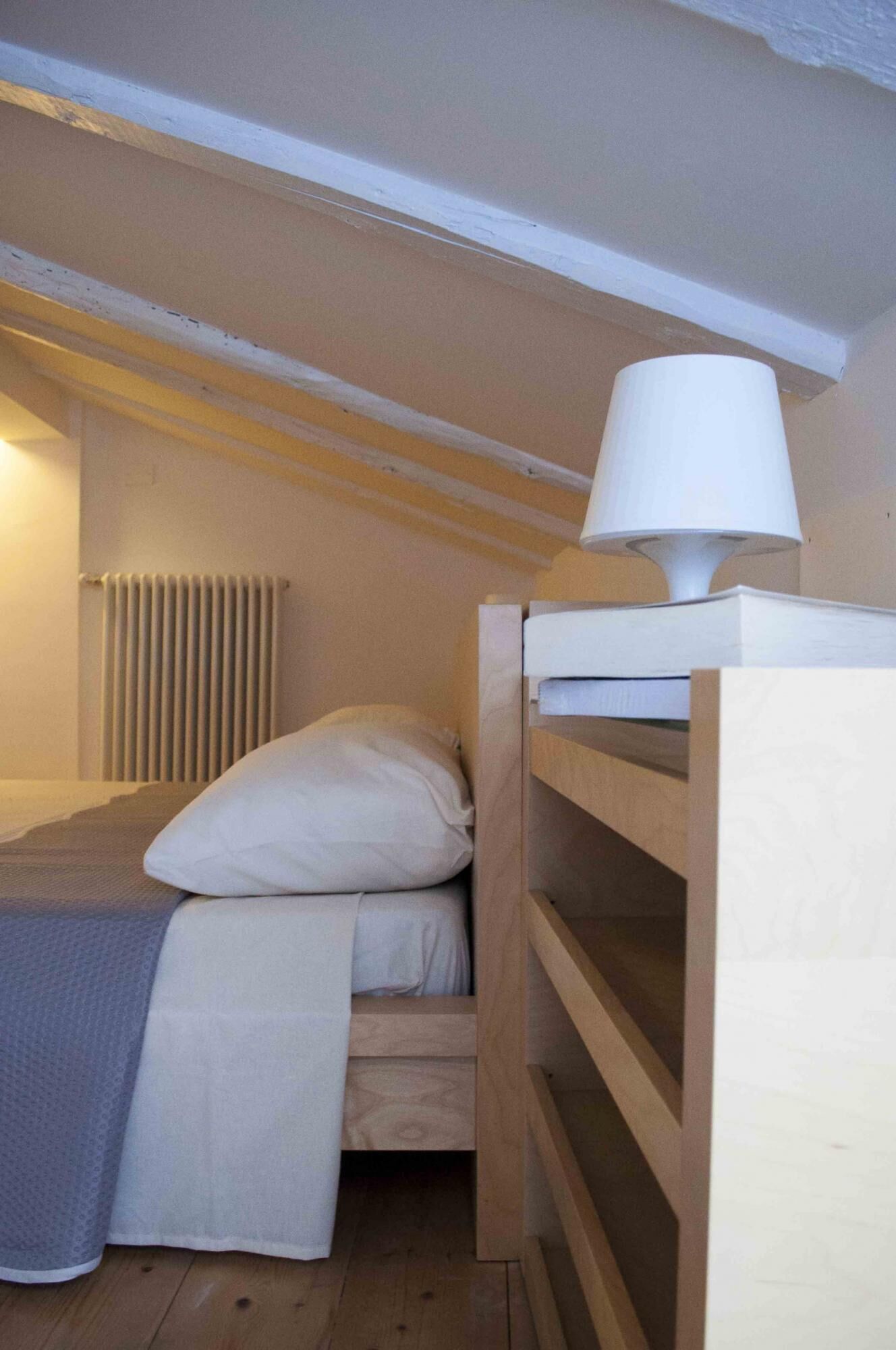 A small, cozy room with a bunk bed, a bedside lamp, and a radiator.