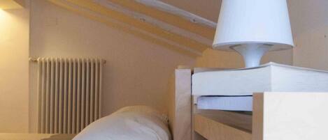A small, cozy room with a bunk bed, a bedside lamp, and a radiator.