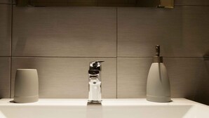 Un bagno moderno con un lavandino bianco, due erogatori di sapone cilindrici e un originale design del rubinetto.