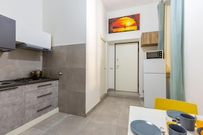 Compact kitchen area with gas stove, microwave, and refrigerator, perfect for preparing meals. A dining table and chairs are also available.
