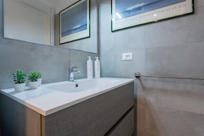 Une salle de bain moderne avec un grand lavabo, deux plantes en pot et des photographies encadrées accrochées au mur.