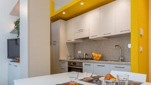 Uma cozinha moderna com armários brancos, uma parede de destaque amarela, uma mesa de jantar com itens de café da manhã e um forno embutido.