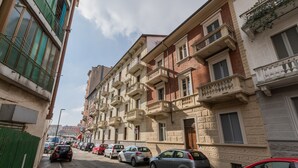 Une rangée d’immeubles résidentiels à plusieurs étages, dotés de balcons, avec des voitures garées et un ciel dégagé.