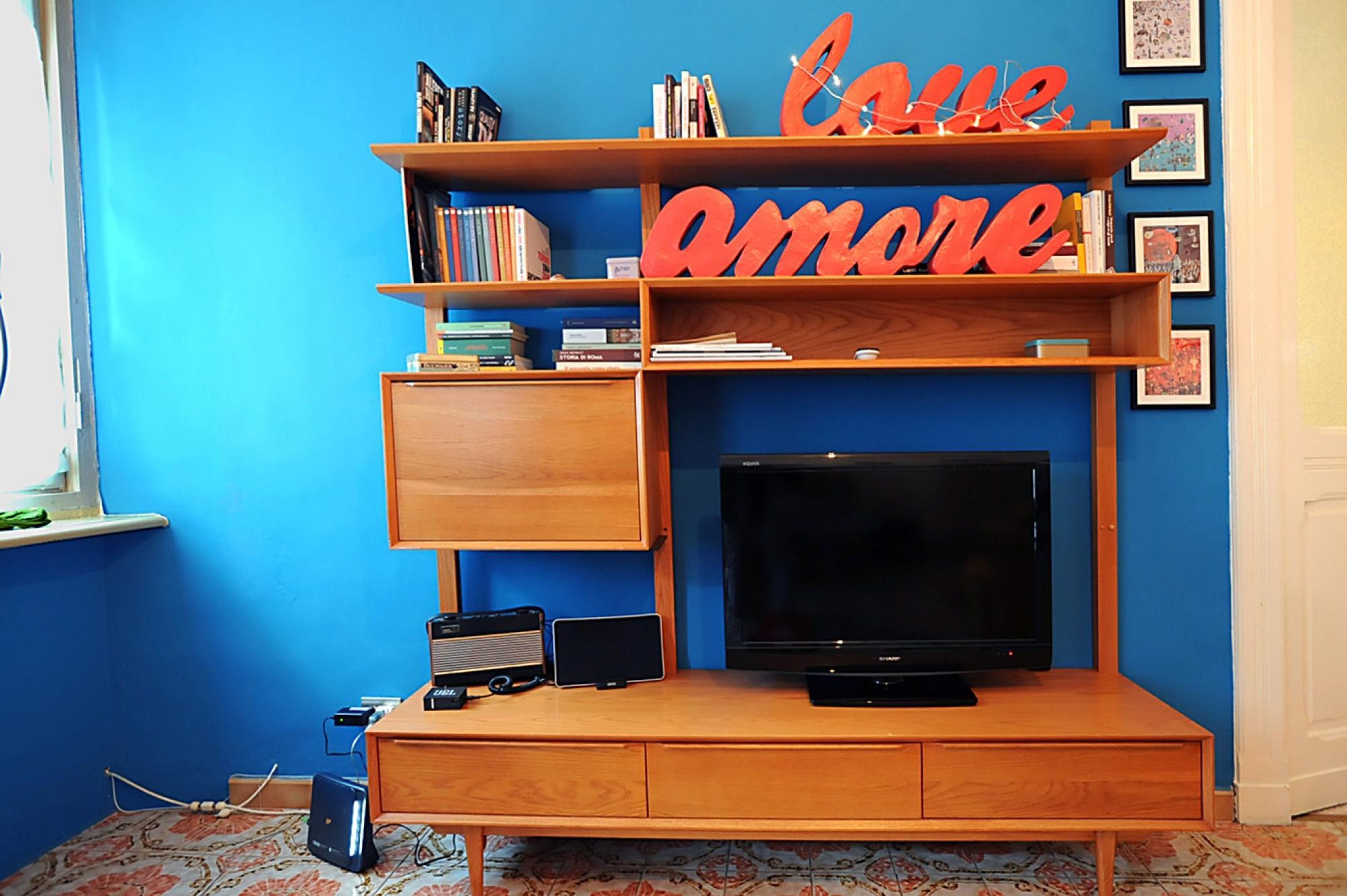 A room with a blue wall, a wooden entertainment unit with a flat-screen TV, books, and decorative items.