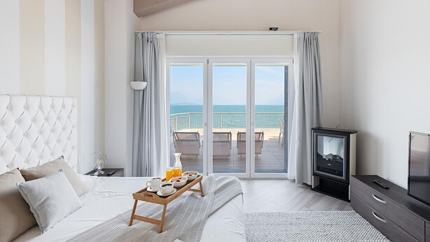 A hotel room with a bed, a TV, a balcony with a view of the sea, and a breakfast tray on the bed.