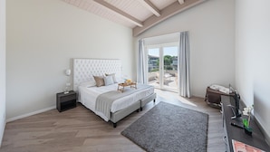 A bedroom with a large bed, a bedside table, a TV, and a view of the outside.