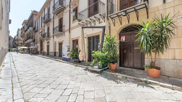 Uma rua de paralelepípedos ladeada por edifícios de vários andares, cada um com varandas e plantas em vasos.
