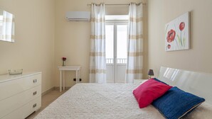 Quarto com cama, mesa de cabeceira, espelho, janela com cortinas e ar condicionado fixado na parede.