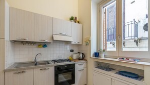 Uma cozinha moderna com armários de madeira clara, fogão a gás, pia e janela com vista para a varanda.