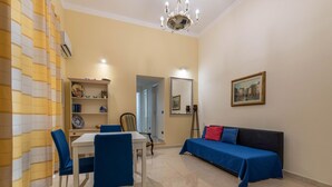 Um quarto com uma mesa de jantar, cadeiras, um sofá, uma estante de livros, um espelho e um quadro na parede.