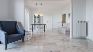A modern living room with a blue armchair, a dining area with a table and chairs, and a white sofa.
